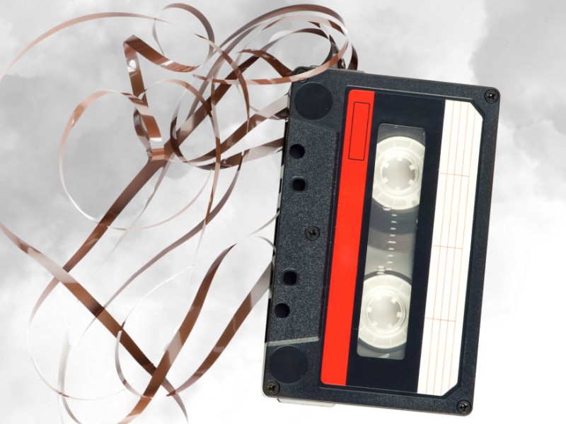 Audiokassette mit herausgezogenem Band vor grauem Hintergrund