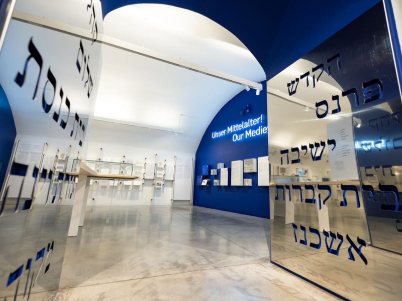 Blick in einen modernen Ausstellungsraum mit blauen Wänden und Schrifttafeln auf Deutsch und Englisch 'Unser Mittelalter! Our Medie'