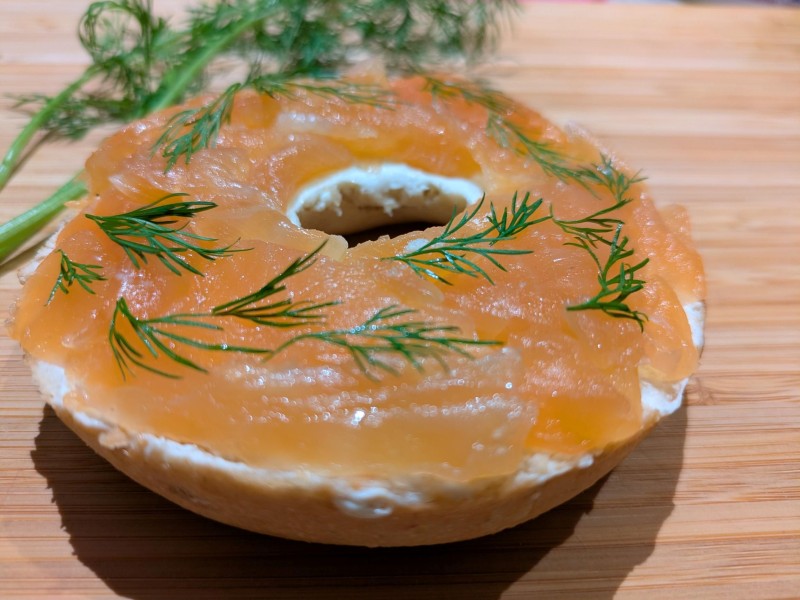 Bagel with cream cheese, smoked salmon, and dill on wooden surface