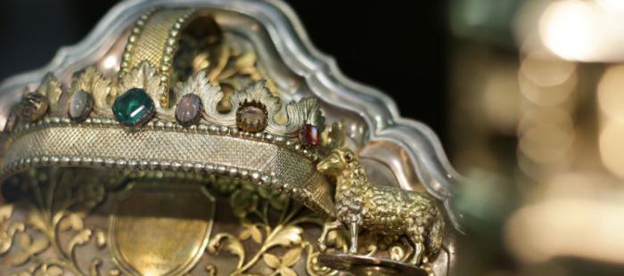 Close-up of an ornate artwork featuring a gold-colored crown with embedded stones and a gold-colored metal sheep